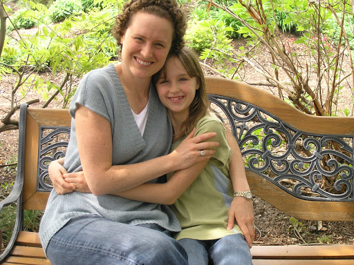 Ashlea and her mother Kristen Milligan, co-founder of Inheritance of Hope, smiling and hugging while sitting on a bench with foliage in the background