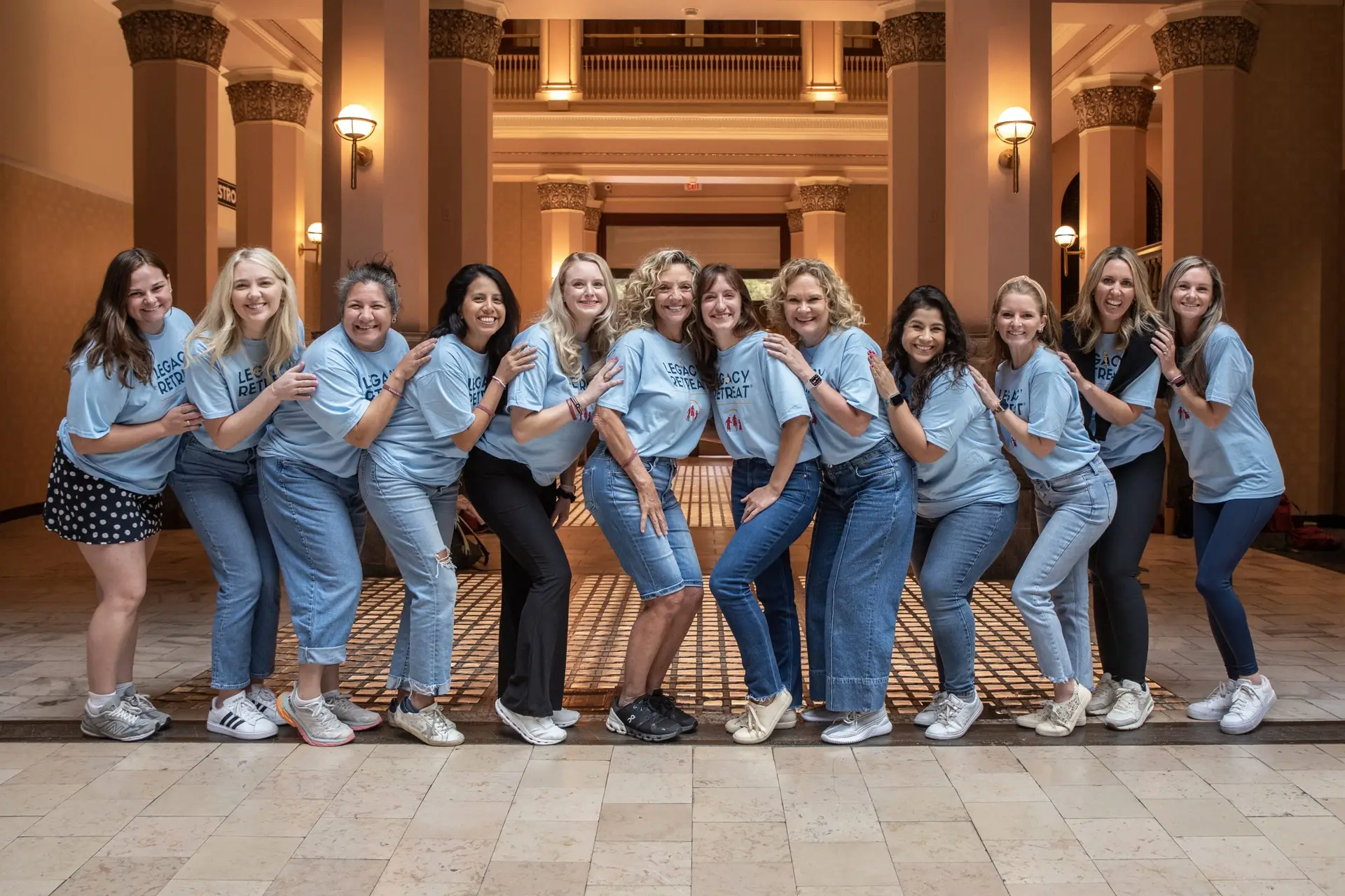 A group of women in a lobby standing in a line smiling