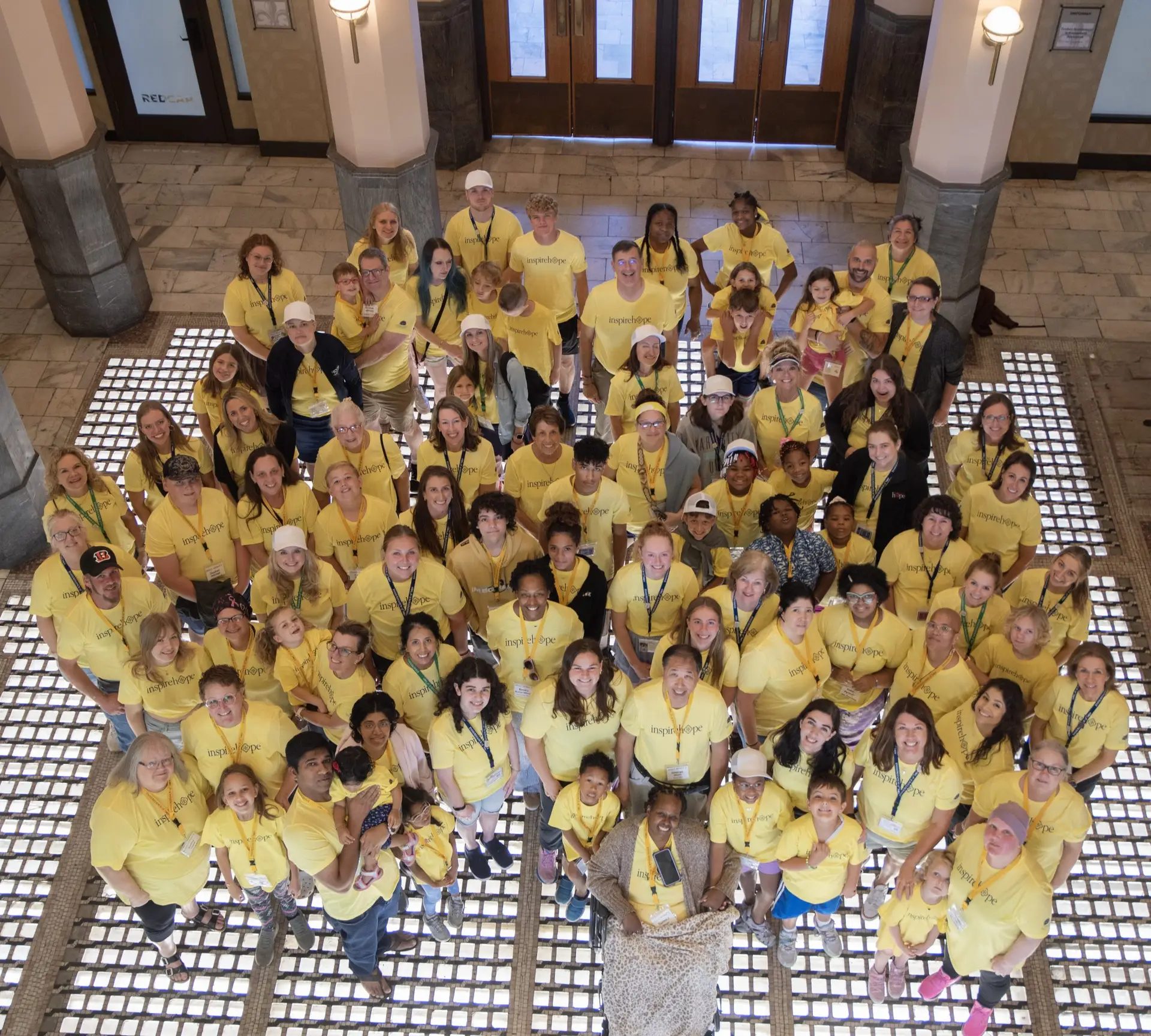 A large group of smiling children and adults wearing yellow shirts standing in a lobby