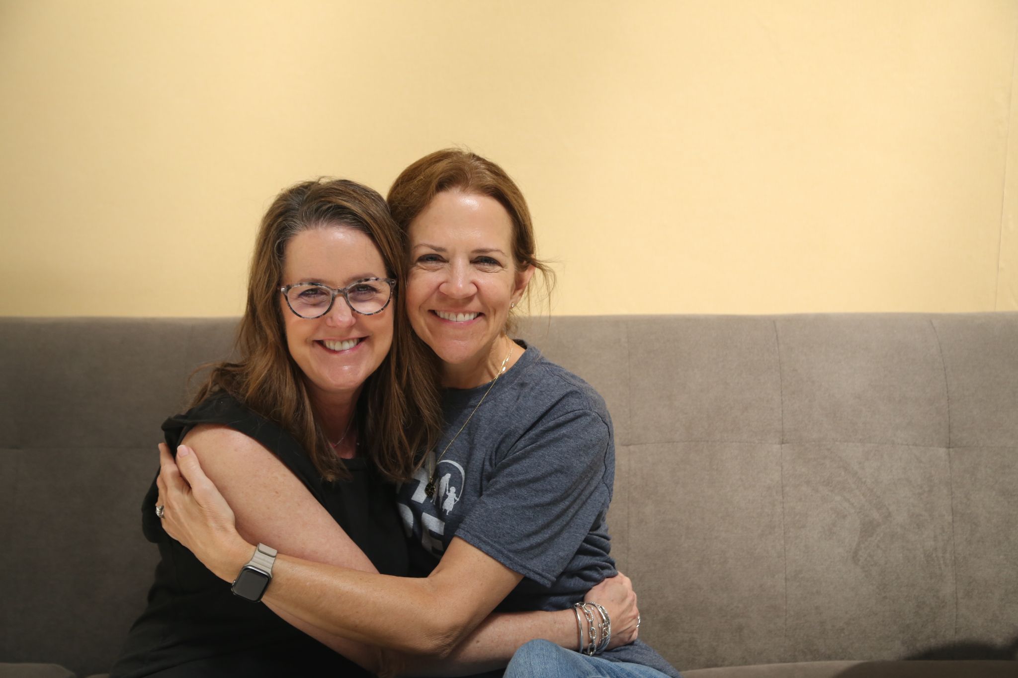Two women hugging and smiling while sitting on a couch
