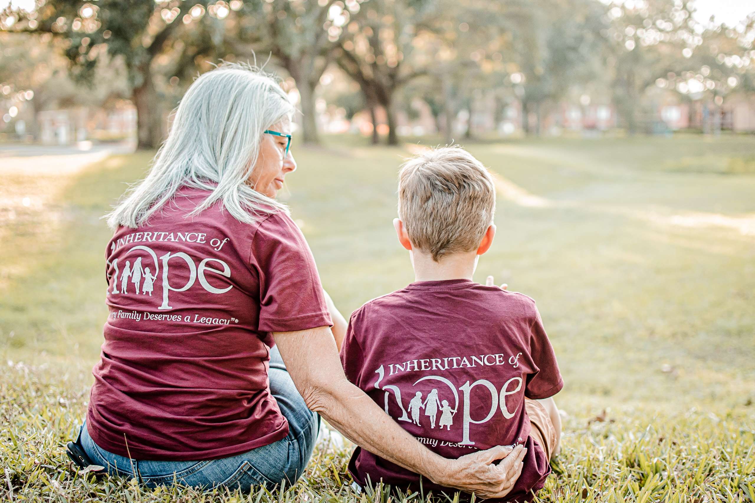 A woman and young child sitting together outdoors, wearing matching Inheritance of Hope shirts.