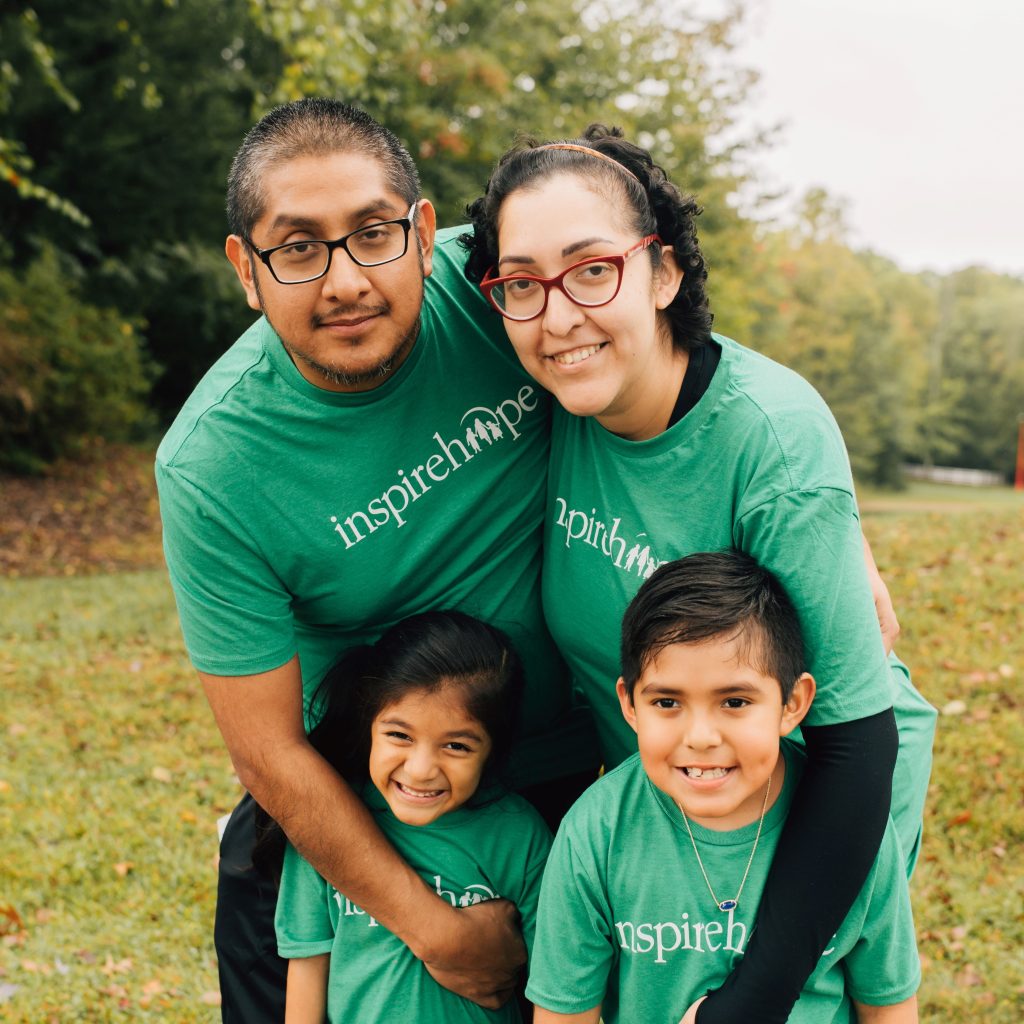 A family in matching green "Inspire Hope" shirts shares a warm embrace at an Inheritance of Hope Legacy Retreat.