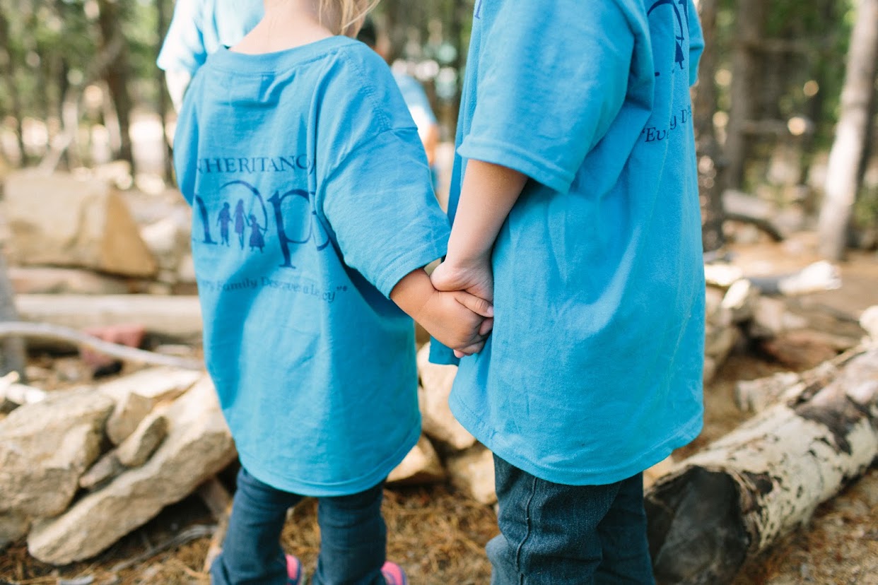 Two young children holding hands and wearing matching blue Inheritance of Hope shirts
