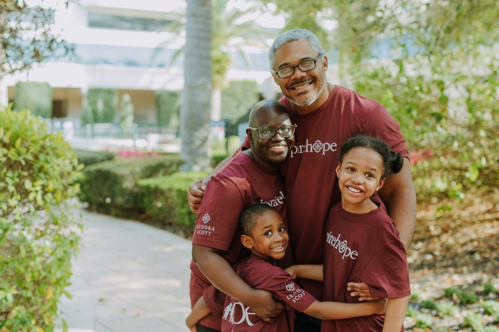 Family smiling and hugging outdoors in matching Inspire Hope shirts.