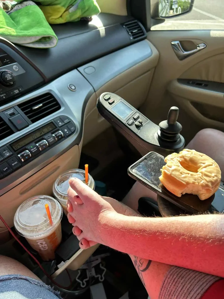 A disabled man and his wife hold hands in the car. In the background are cups of iced coffee.