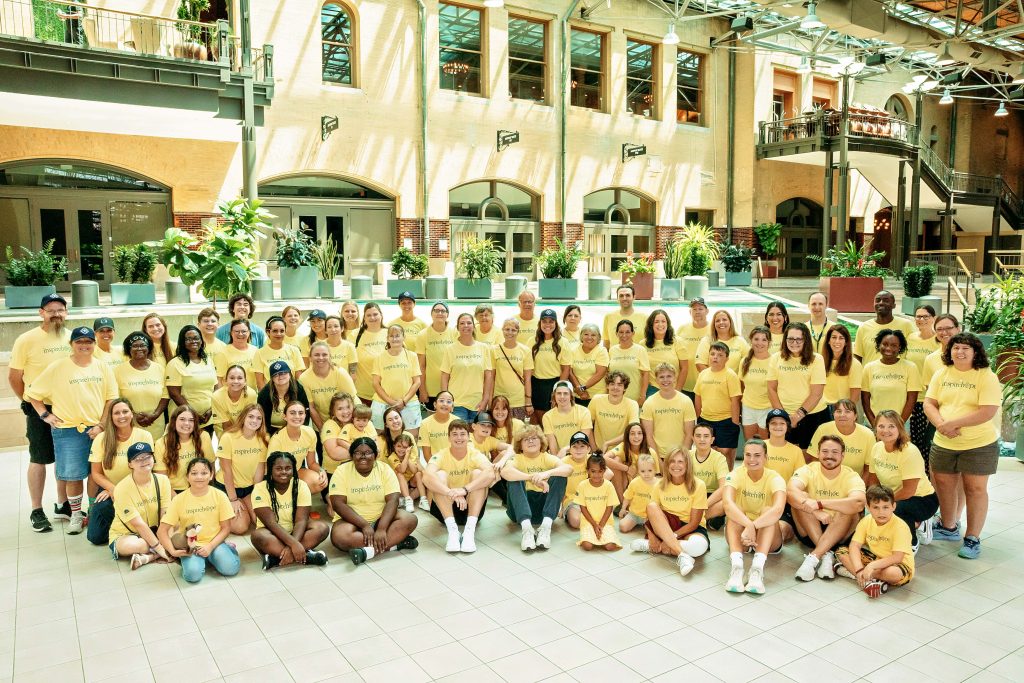 A large group of families and volunteers wearing yellow Inheritance of Hope t-shirts pose for a photo