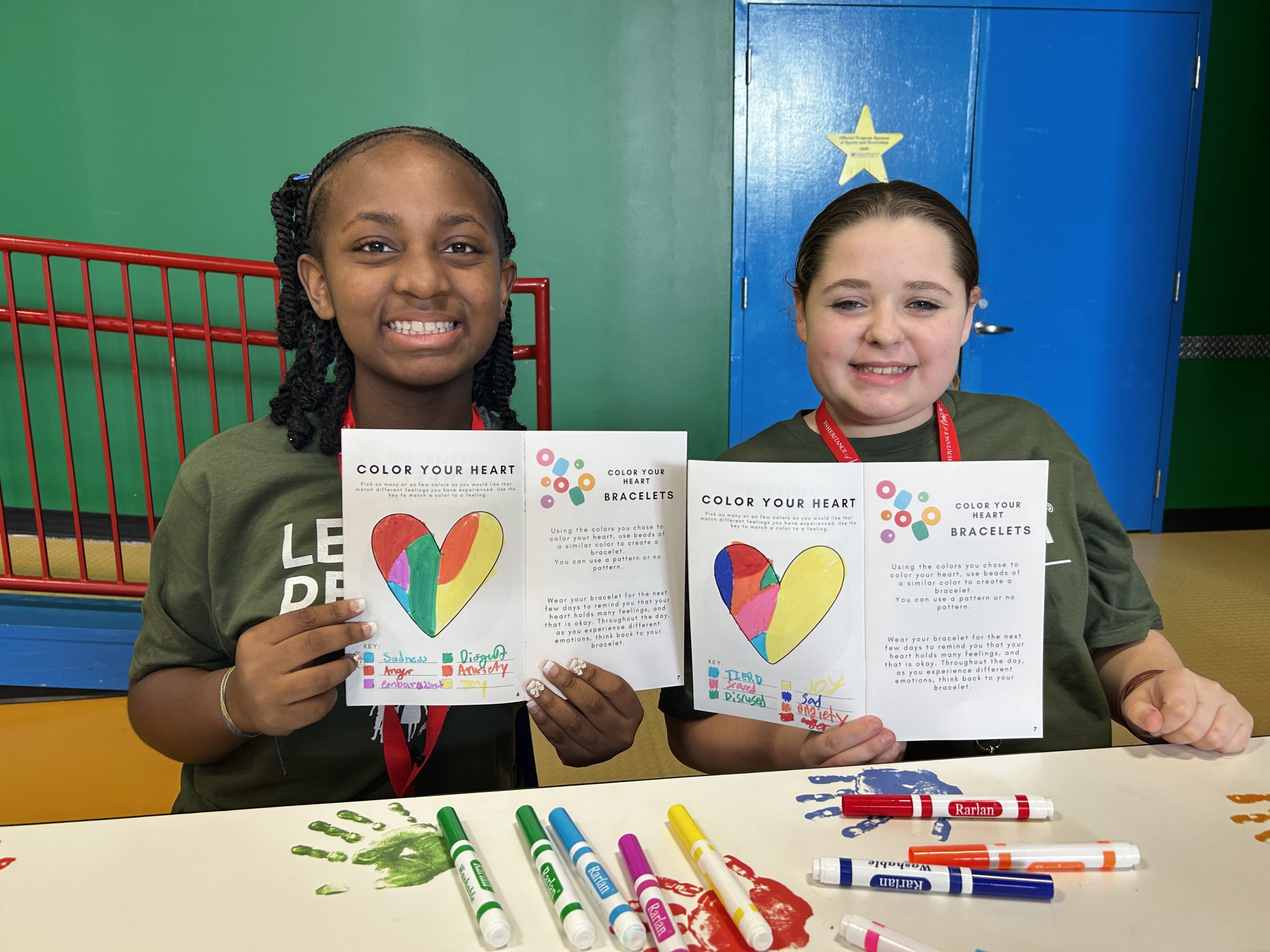 Two girls holding a workbook with a heart. The heart is colored in with various colors representing different feelings.