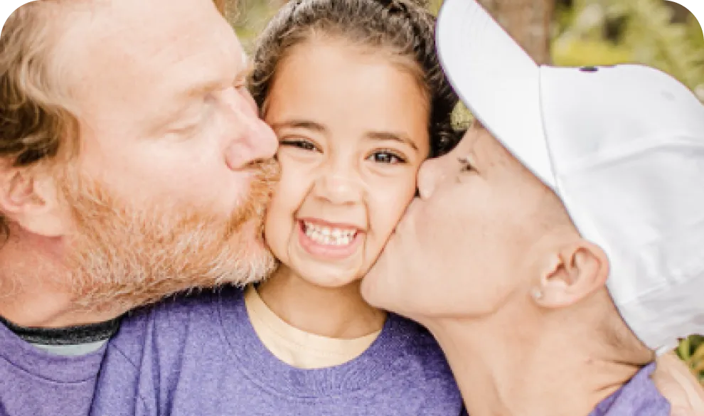 A mother and father kissing their child on the cheek