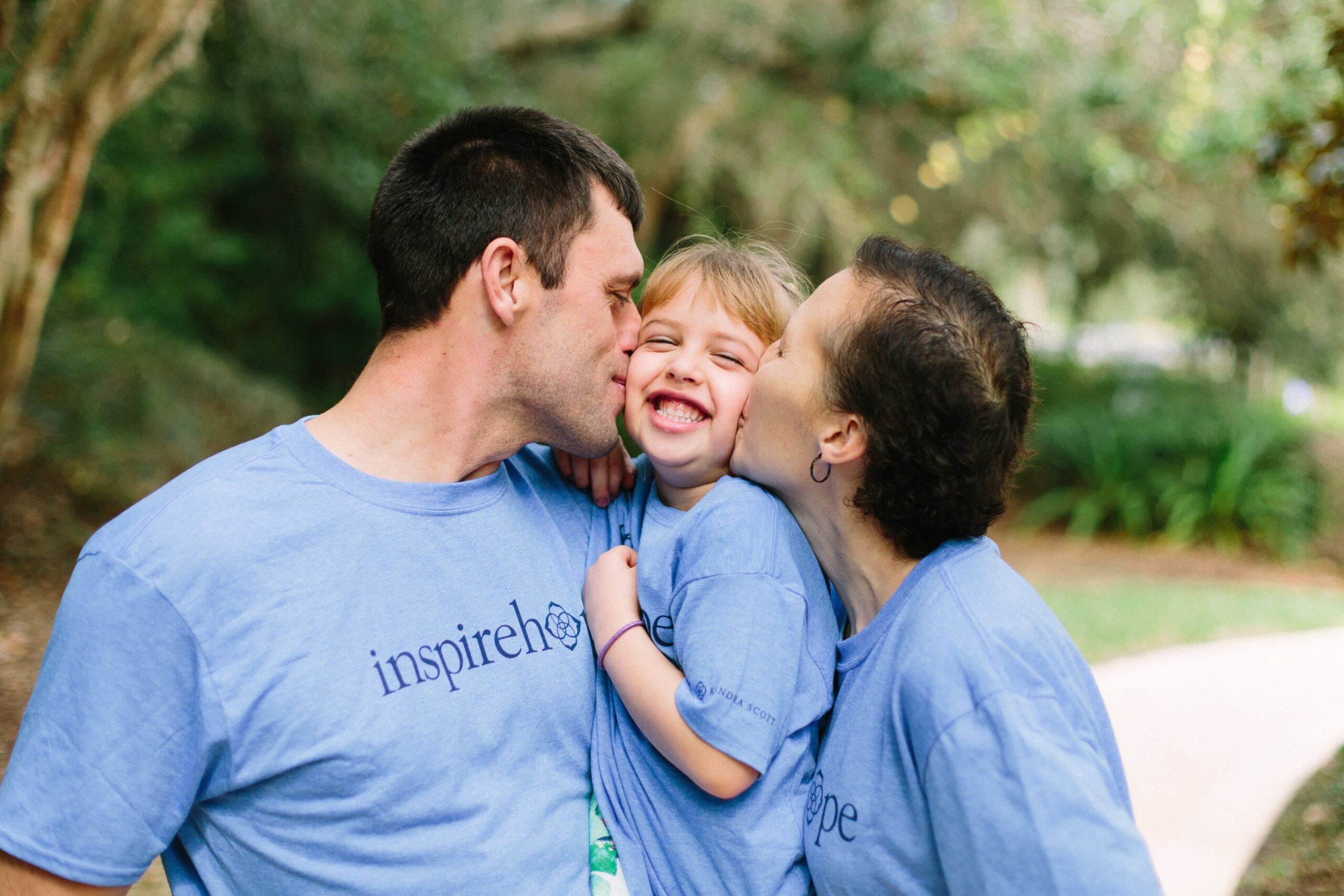 Two family members kissing smiling little girl on the cheeks.