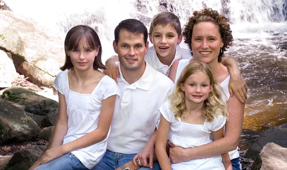 family-card Kristen Milligan posing for a scenic photo in front of a waterfall with her husband and three children