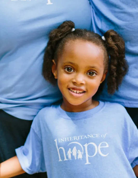 A young girl smiling and standing in front of two adults
