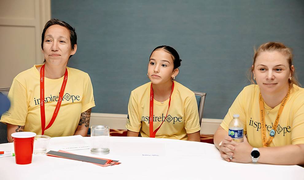 Two women and a young girl wearing yellow t-shirts sitting at a meeting table
