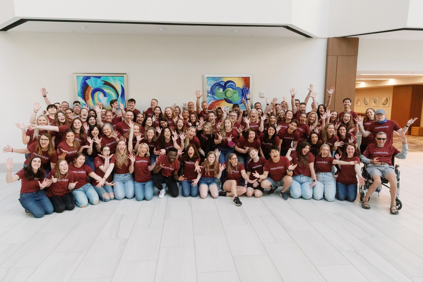 “A moment of pure joy.” A large group of Inheritance of Hope members wearing red t-shirts smiling for a picture inside a facility