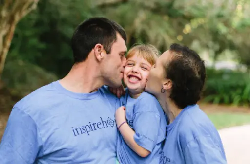 Parents in charity shirts kissing laughing child