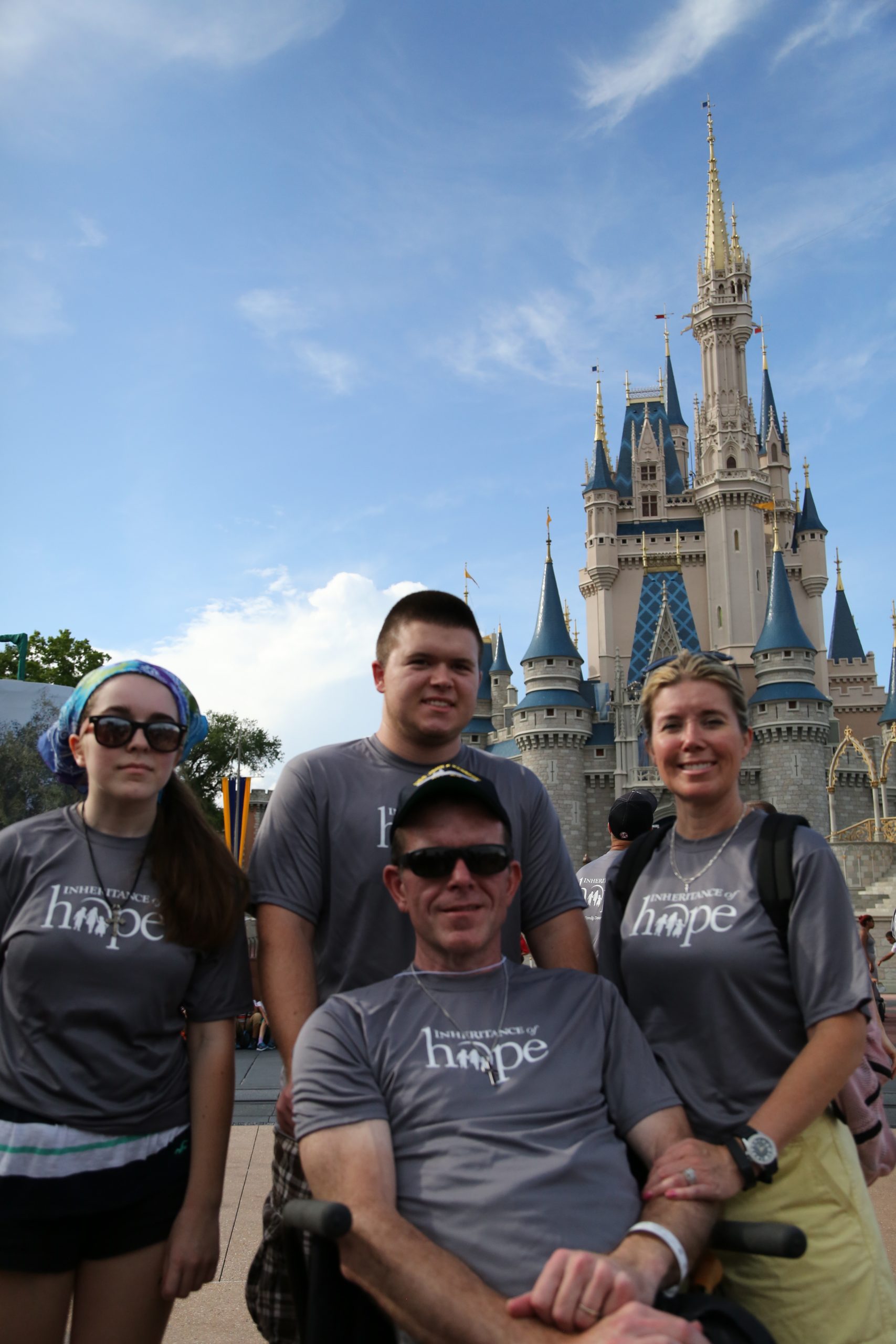 A family in matching Inheritance of Hope shirts poses in front of Cinderella Castle at Disney World.
