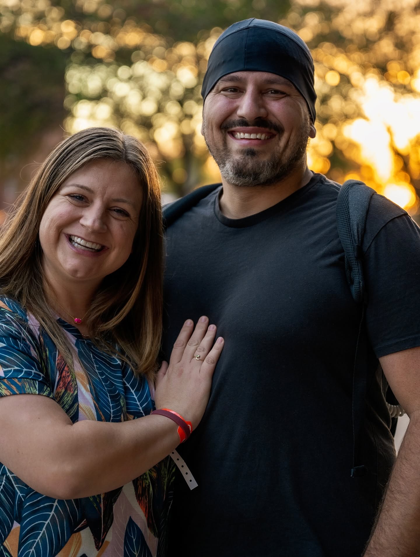 A smiling couple stands together outdoors at sunset