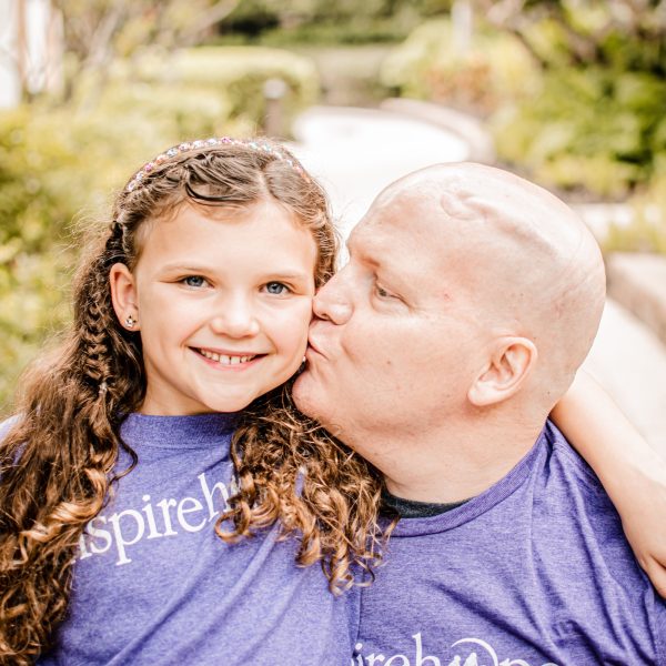 Young dad with cancer kissing his daughter on the cheek.